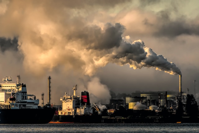 Fossil fuel industrial installations spew smoke into the sky at sunset